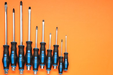 Photo of Set of screwdrivers on orange background, flat lay. Space for text