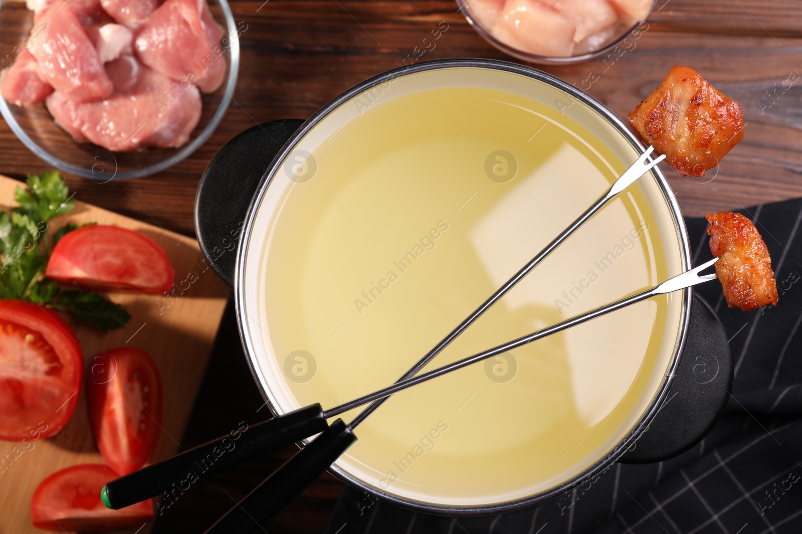 Photo of Fondue pot, forks with fried meat pieces and other products on wooden table, flat lay