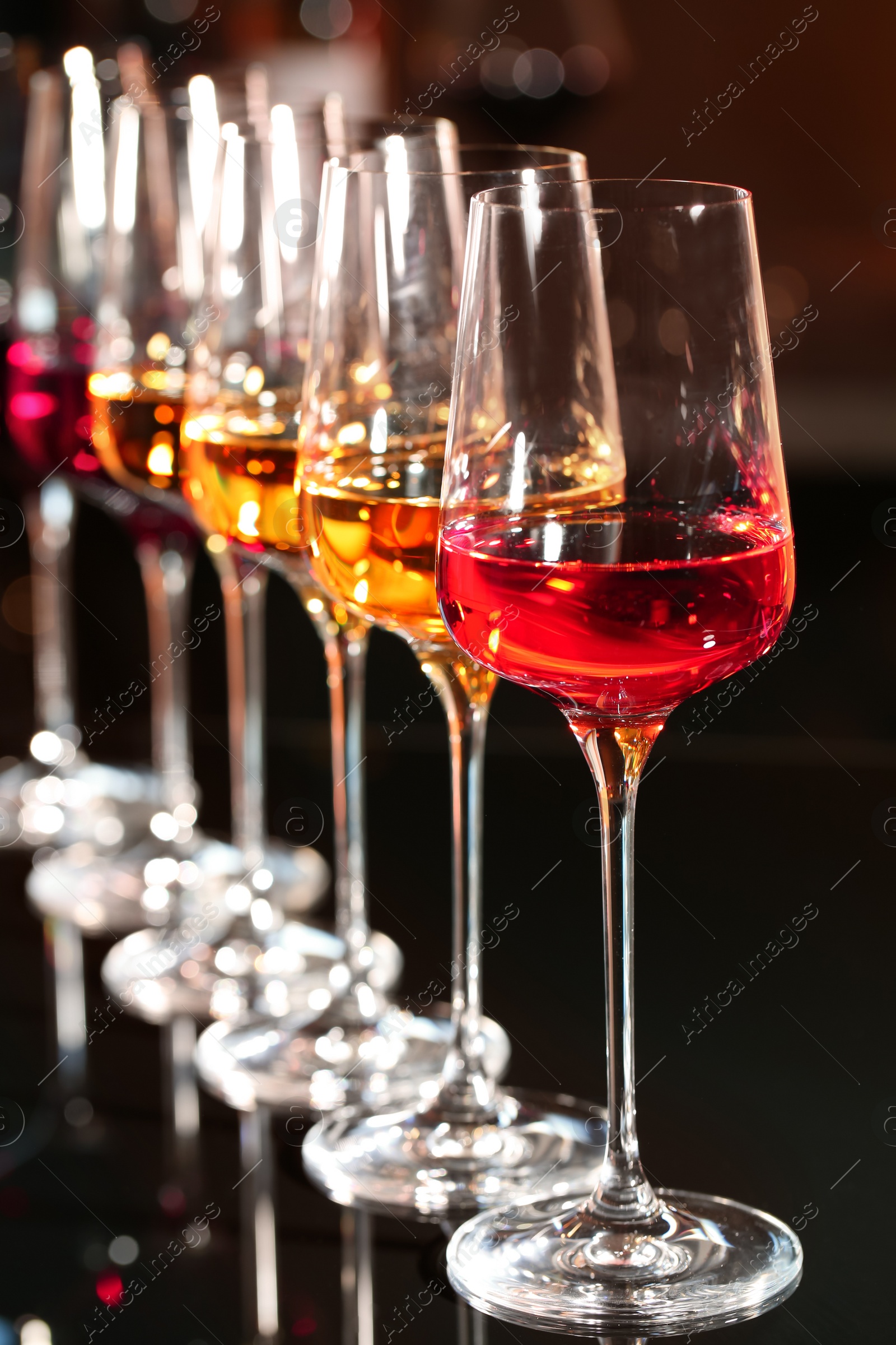 Photo of Row of glasses with different wines on table against blurred background