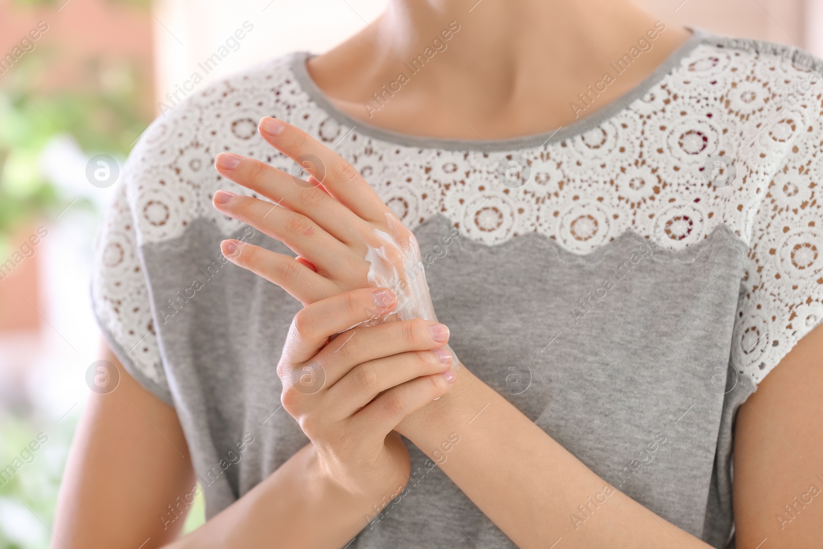 Photo of Young woman applying cream on her hands, closeup