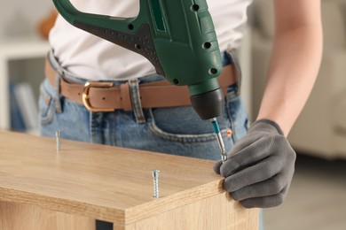 Photo of Woman with electric screwdriver assembling furniture indoors, closeup