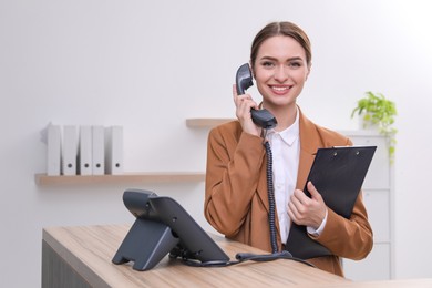 Female receptionist with clipboard talking on phone at workplace