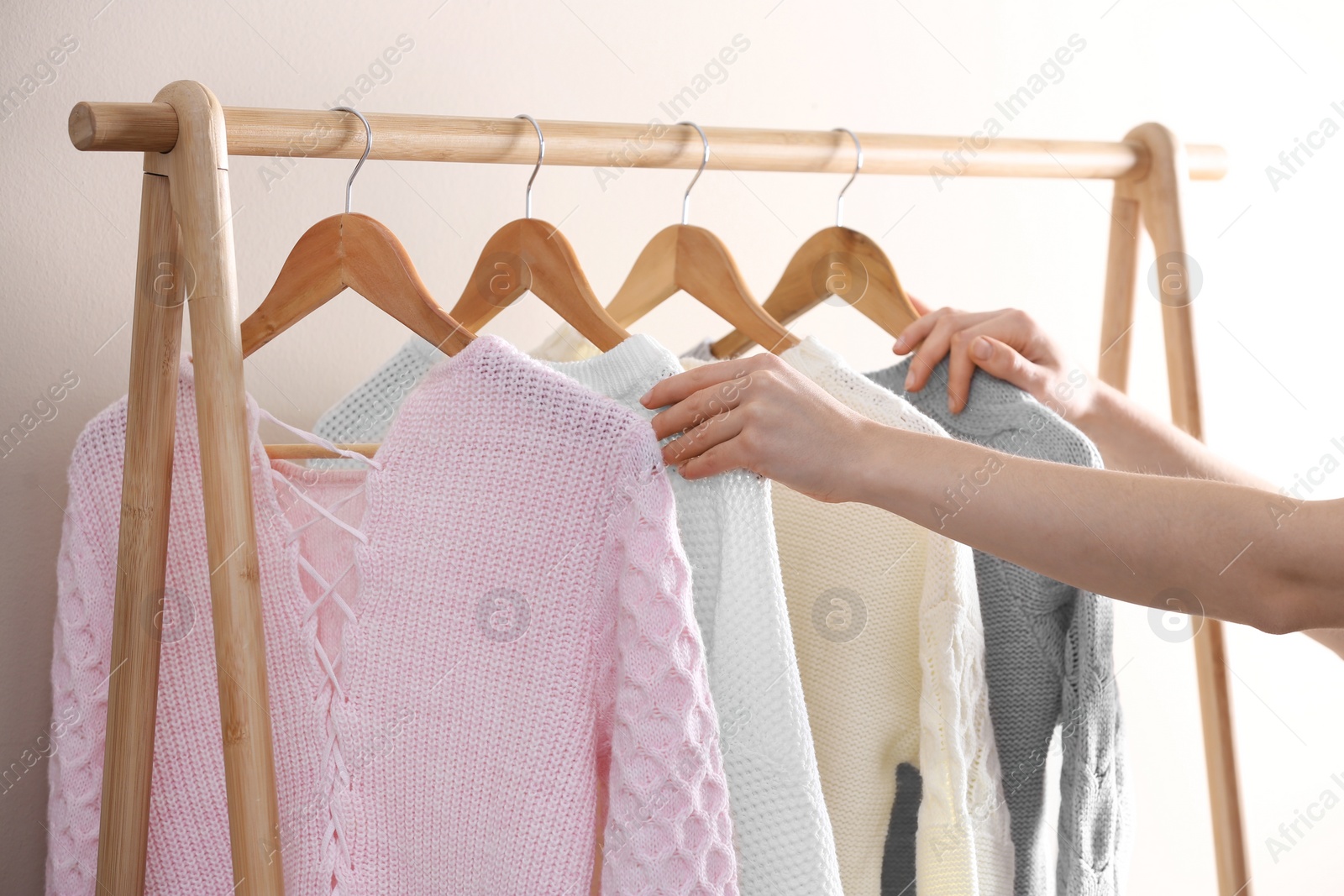 Photo of Woman choosing warm sweater on rack near light wall, closeup