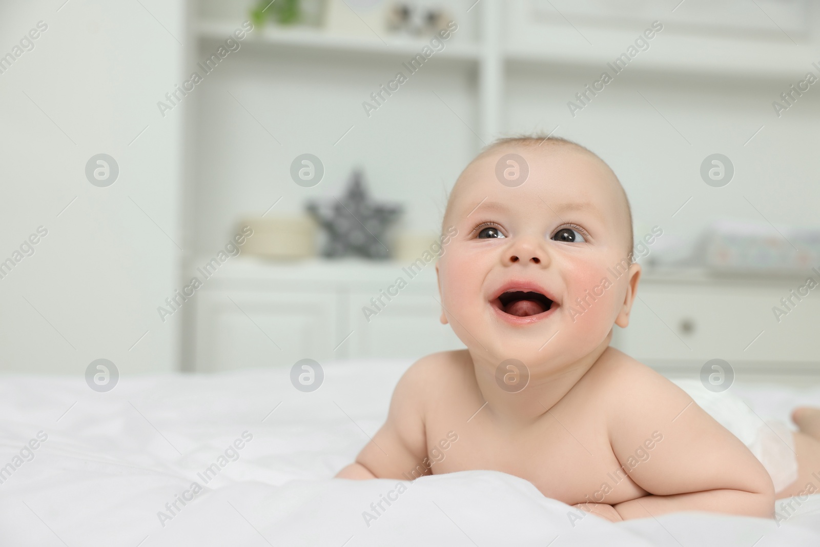 Photo of Cute baby lying on white bed at home, space for text