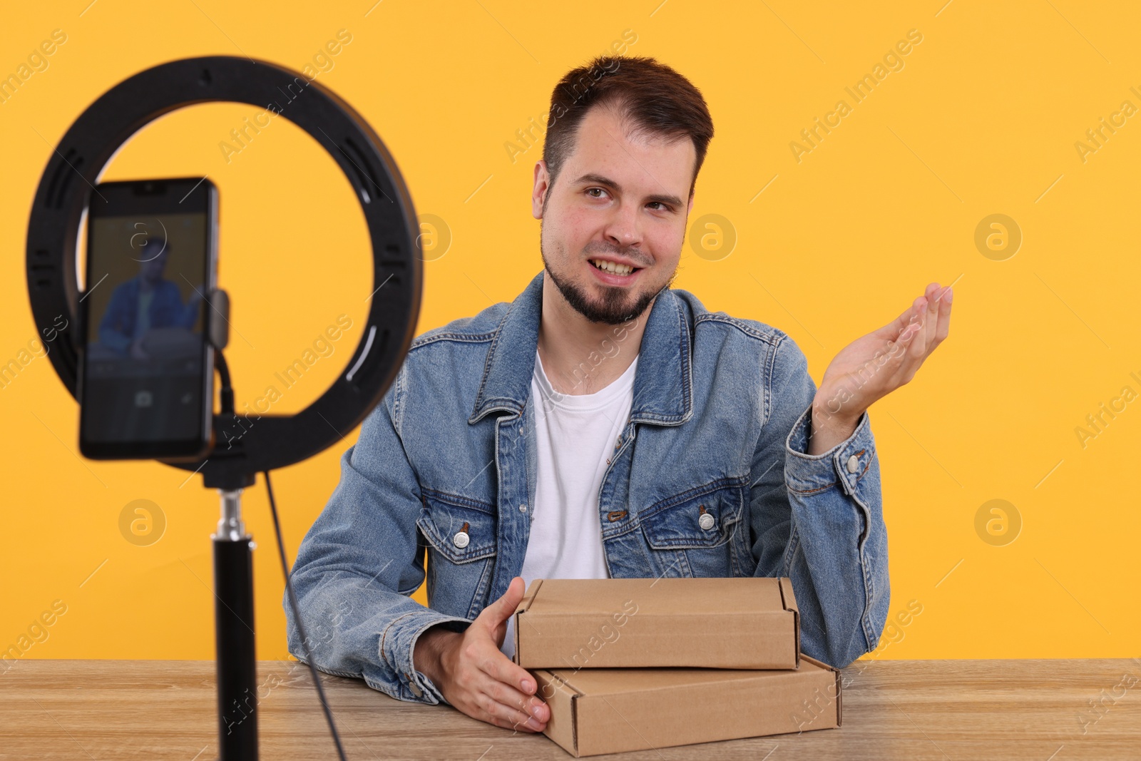 Photo of Smiling fashion blogger with parcels recording video at table against orange background