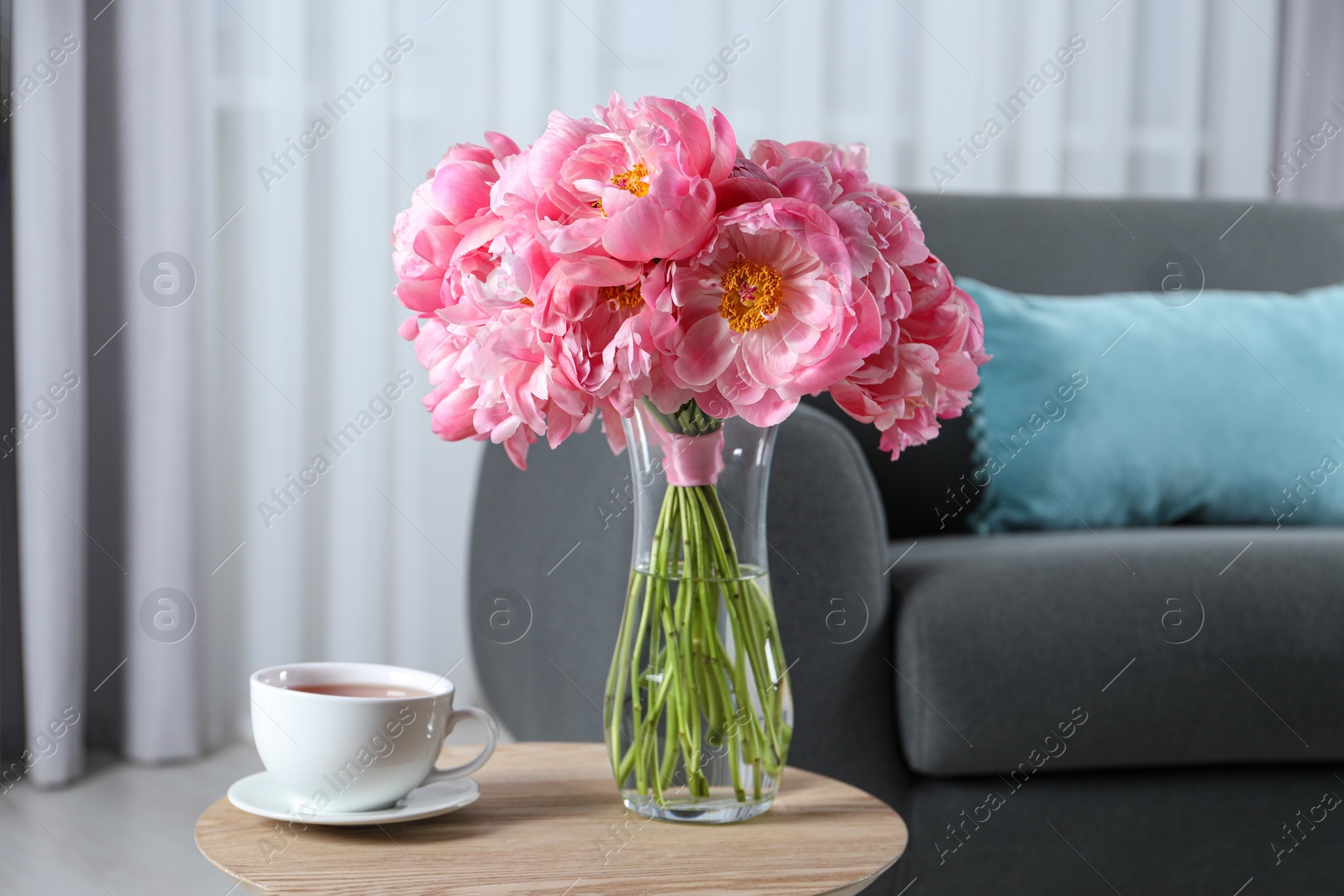 Photo of Beautiful bouquet of pink peonies in vase and cup with drink on wooden table indoors