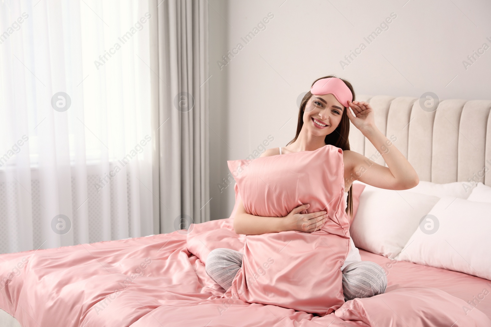 Photo of Young woman hugging pillow on comfortable bed with silky linens