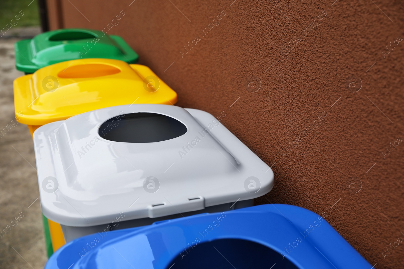 Photo of Many color recycling bins near brown wall outdoors, closeup