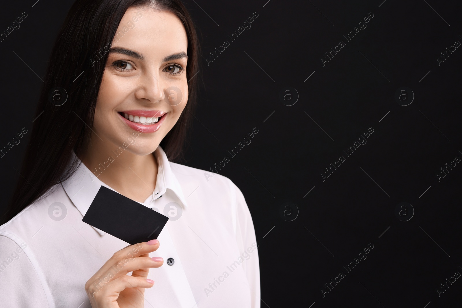 Photo of Happy woman holding blank business card on black background. Space for text