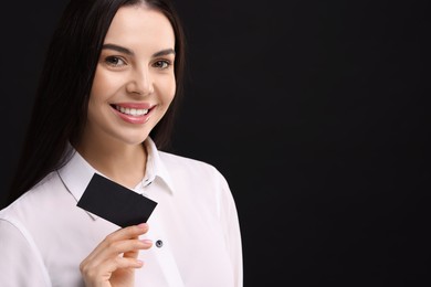 Happy woman holding blank business card on black background. Space for text