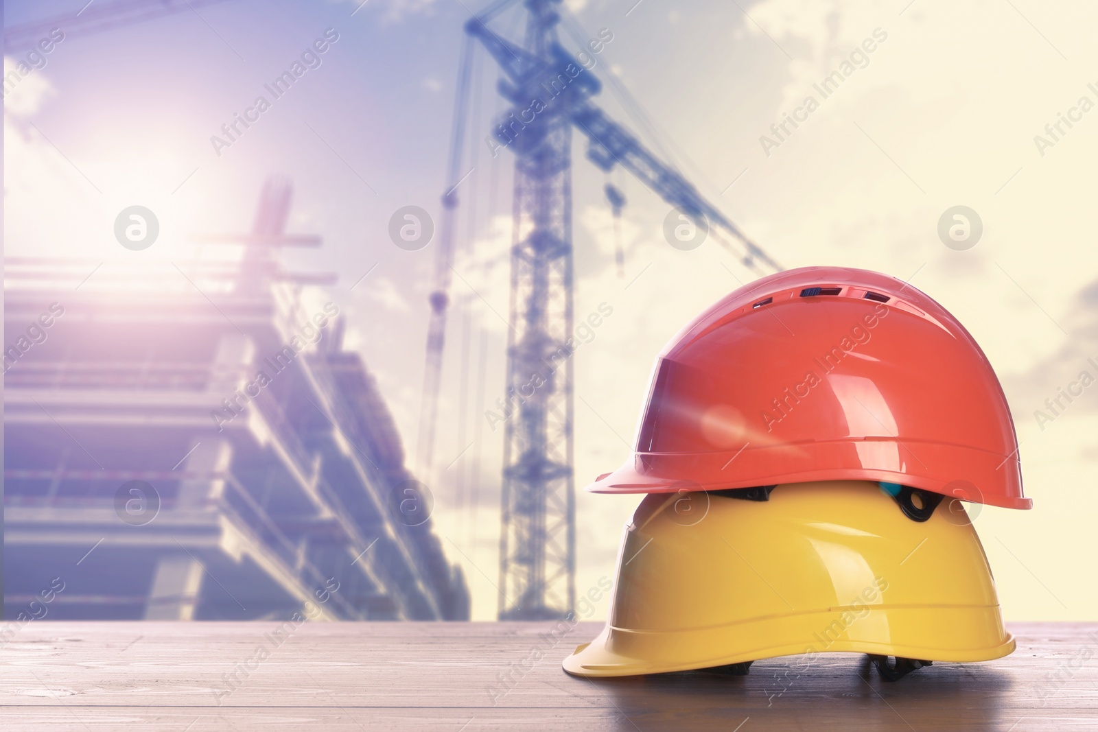 Image of Hard hats on wooden surface at construction site with unfinished building. Space for text 