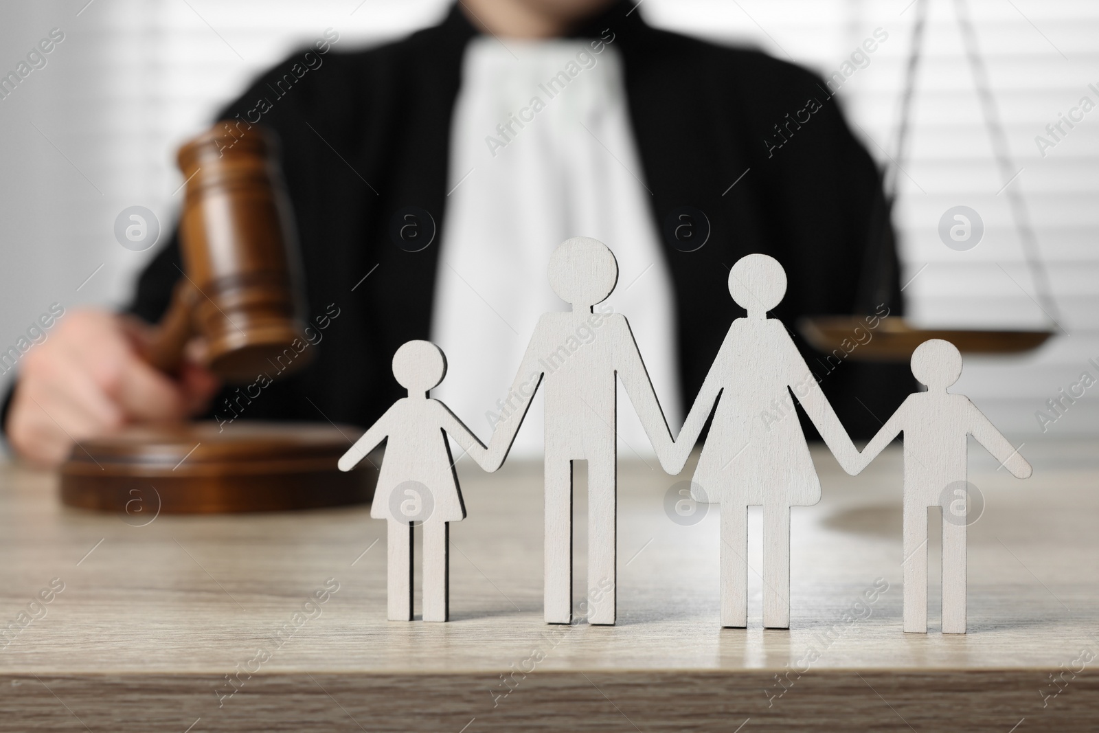 Photo of Family law. Judge with gavel sitting at wooden table, focus on figure of parents and children