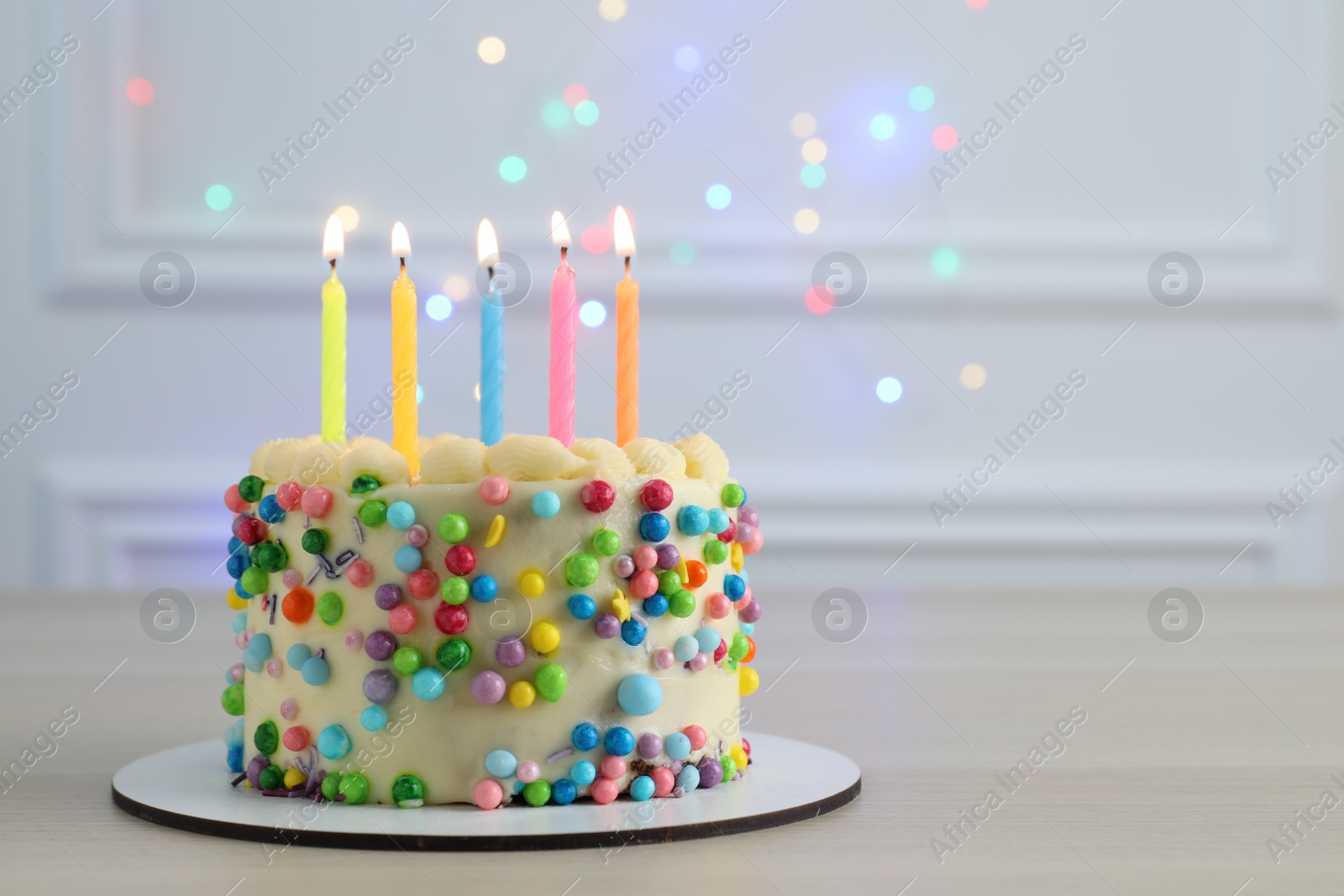 Photo of Cute bento cake with tasty cream and burning candles on white wooden table. Space for text