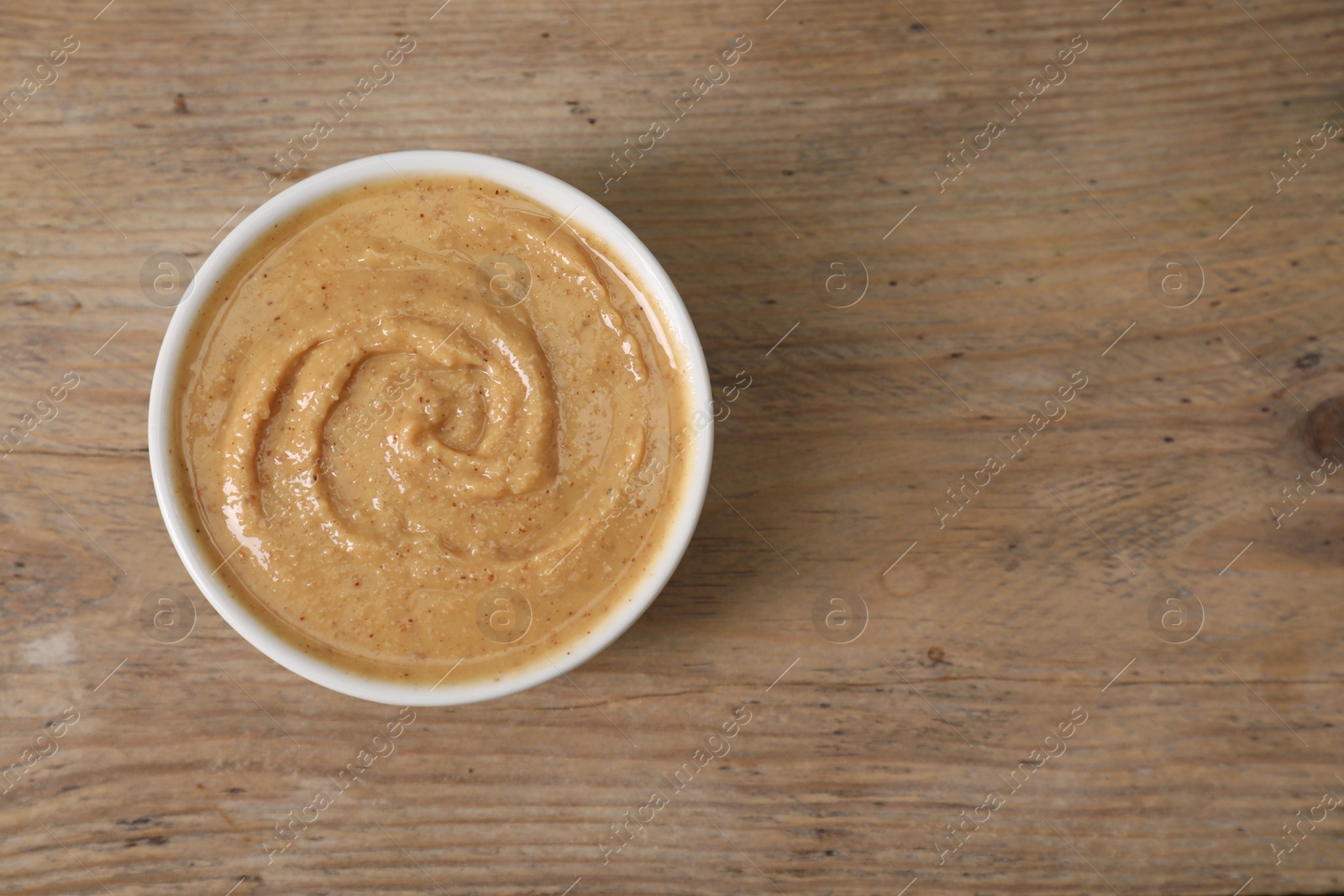 Photo of Delicious nut butter in bowl on wooden table, top view. Space for text