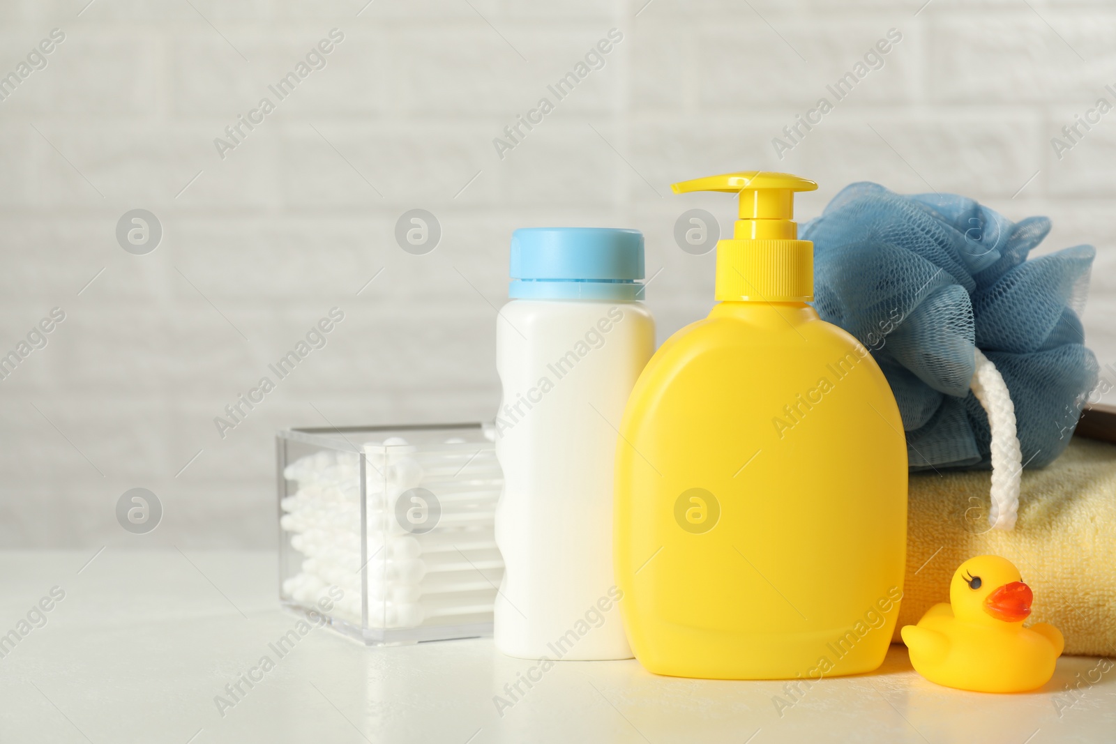 Photo of Baby cosmetic products, bath duck, cotton swabs and towel on white table against brick wall. Space for text