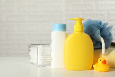 Baby cosmetic products, bath duck, cotton swabs and towel on white table against brick wall. Space for text