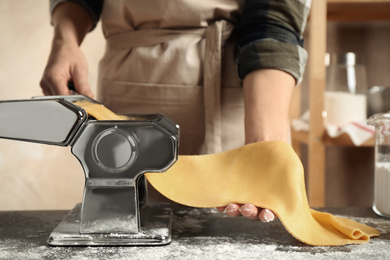 Photo of Woman preparing dough with pasta maker machine at table, closeup