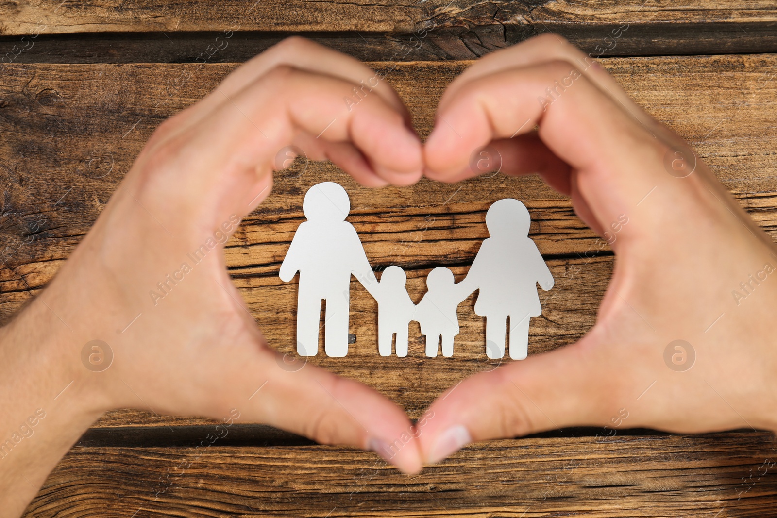 Photo of Man making heart with his hands around paper family figure on wooden background, top view