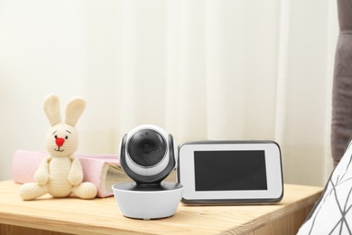 Photo of Baby monitor with camera, photo album and toy on table in room. Video nanny