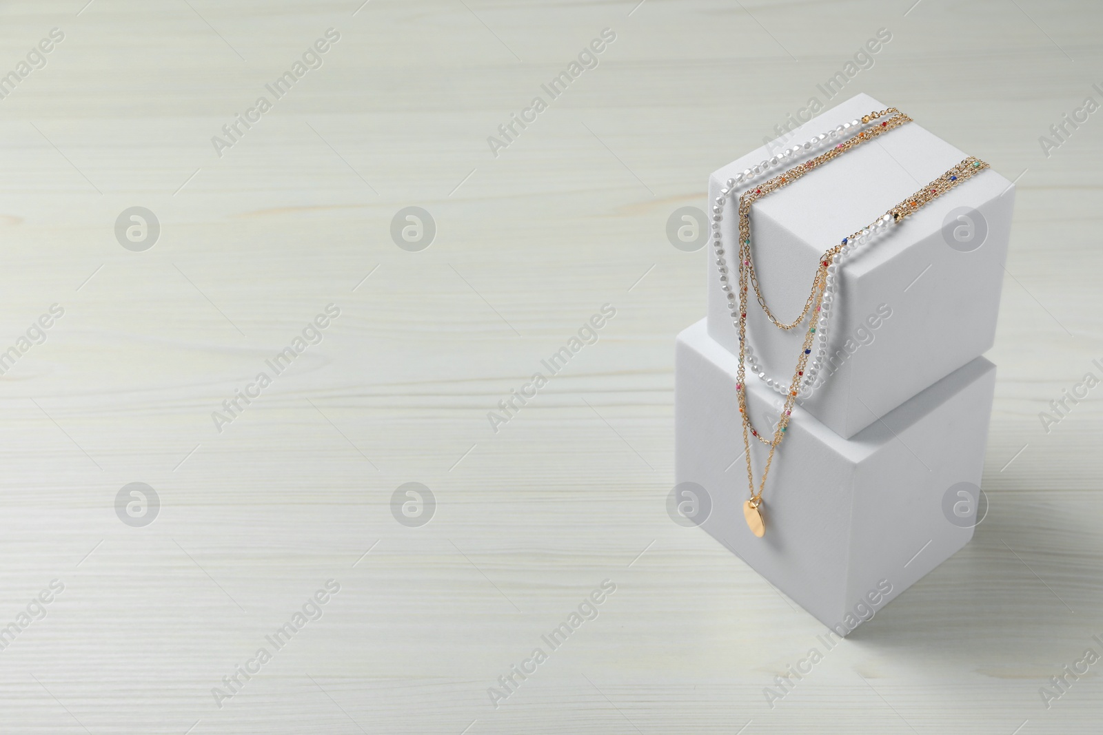 Photo of Stylish presentation of necklaces on podiums on white wooden table, space for text