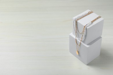 Photo of Stylish presentation of necklaces on podiums on white wooden table, space for text