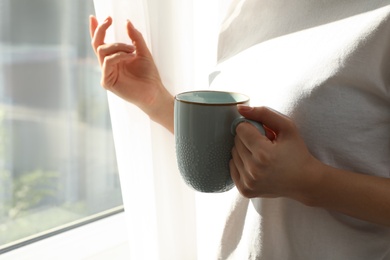 Woman with blue cup near window at home, closeup