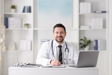 Smiling doctor with laptop at table in clinic. Online medicine