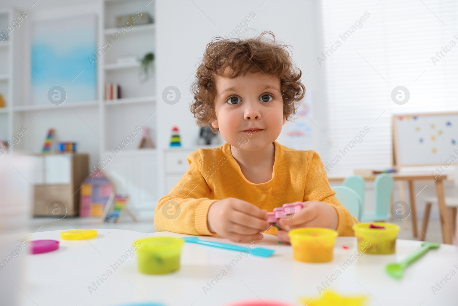 Photo of Cute little boy modeling from plasticine at white table in kindergarten