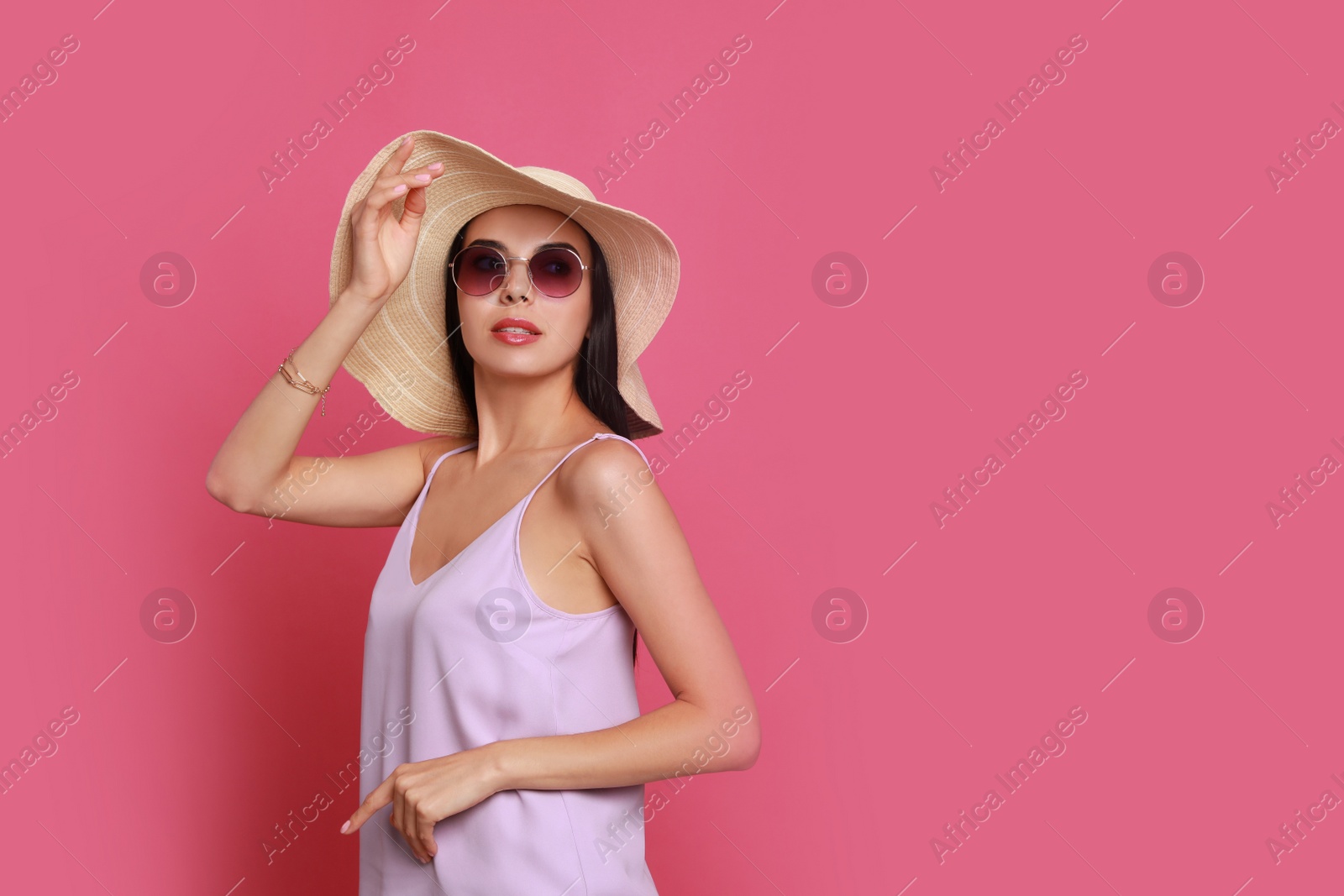 Photo of Beautiful young woman with straw hat and stylish sunglasses on pink background. Space for text