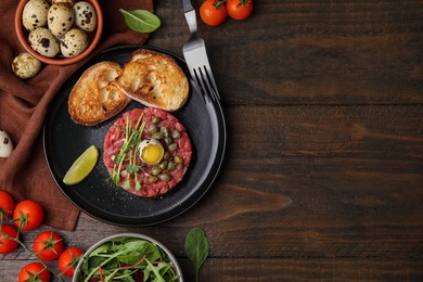 Photo of Tasty beef steak tartare served with quail egg and other accompaniments on wooden table, flat lay. Space for text