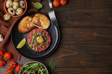 Tasty beef steak tartare served with quail egg and other accompaniments on wooden table, flat lay. Space for text