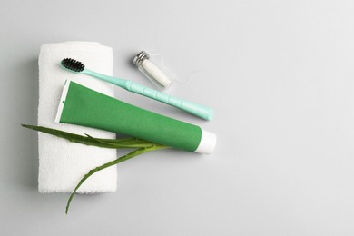 Tube of toothpaste, toothbrush, dental floss, towel and fresh aloe on light grey background, flat lay. Space for text