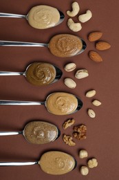 Photo of Tasty nut butters in spoons and raw nuts on brown table, flat lay