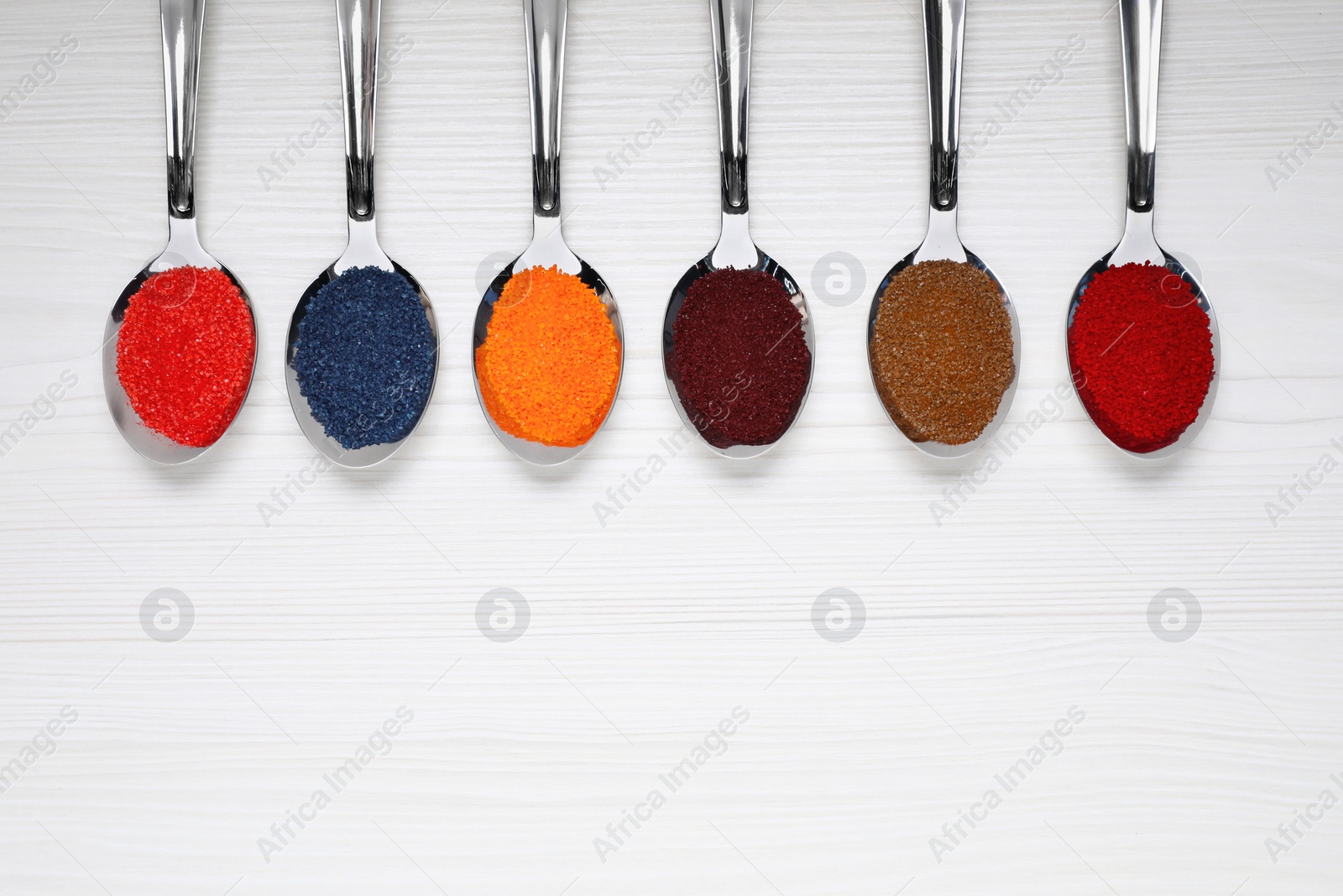 Photo of Spoons with different food coloring on white wooden table, flat lay. Space for text