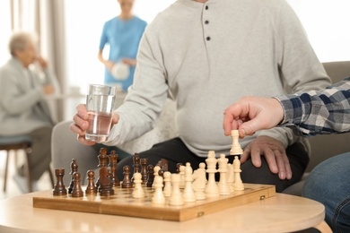 Photo of Elderly men playing chess at nursing home, closeup. Assisting senior people