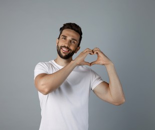 Photo of Happy man making heart with hands on grey background