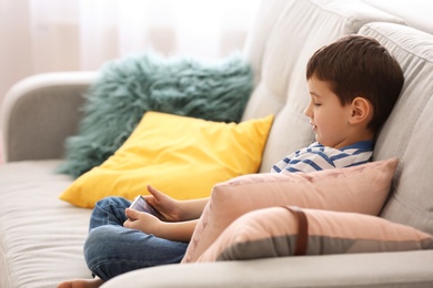 Photo of Cute little boy with mobile phone on sofa at home