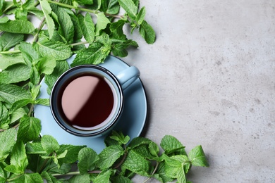 Photo of Cup with hot aromatic mint tea and fresh leaves on grey table, flat lay. Space for text