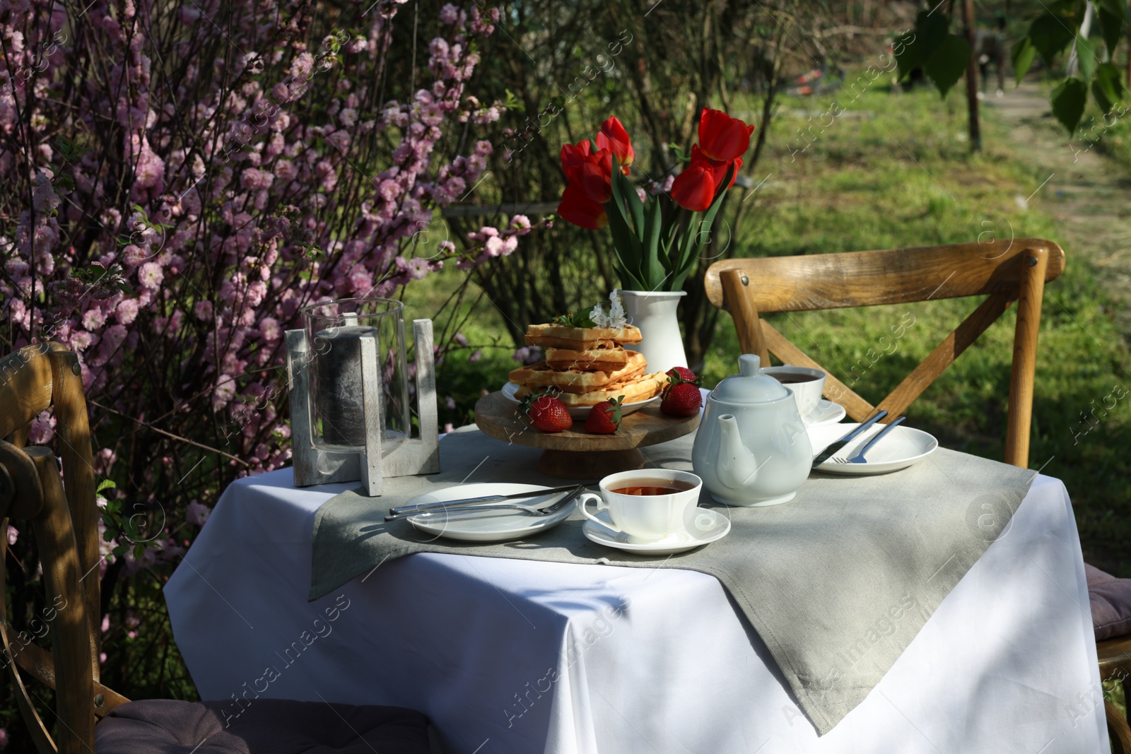 Photo of Beautiful bouquet of tulips and freshly baked waffles on table served for tea drinking in garden