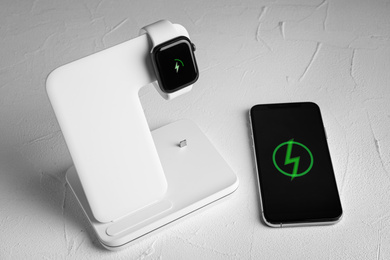 Photo of Smartwatch charging with wireless pad and mobile phone on white stone table