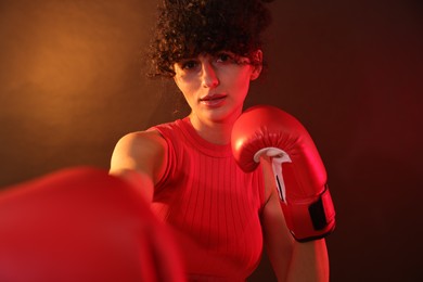 Beautiful young woman with boxing gloves on color background in neon lights