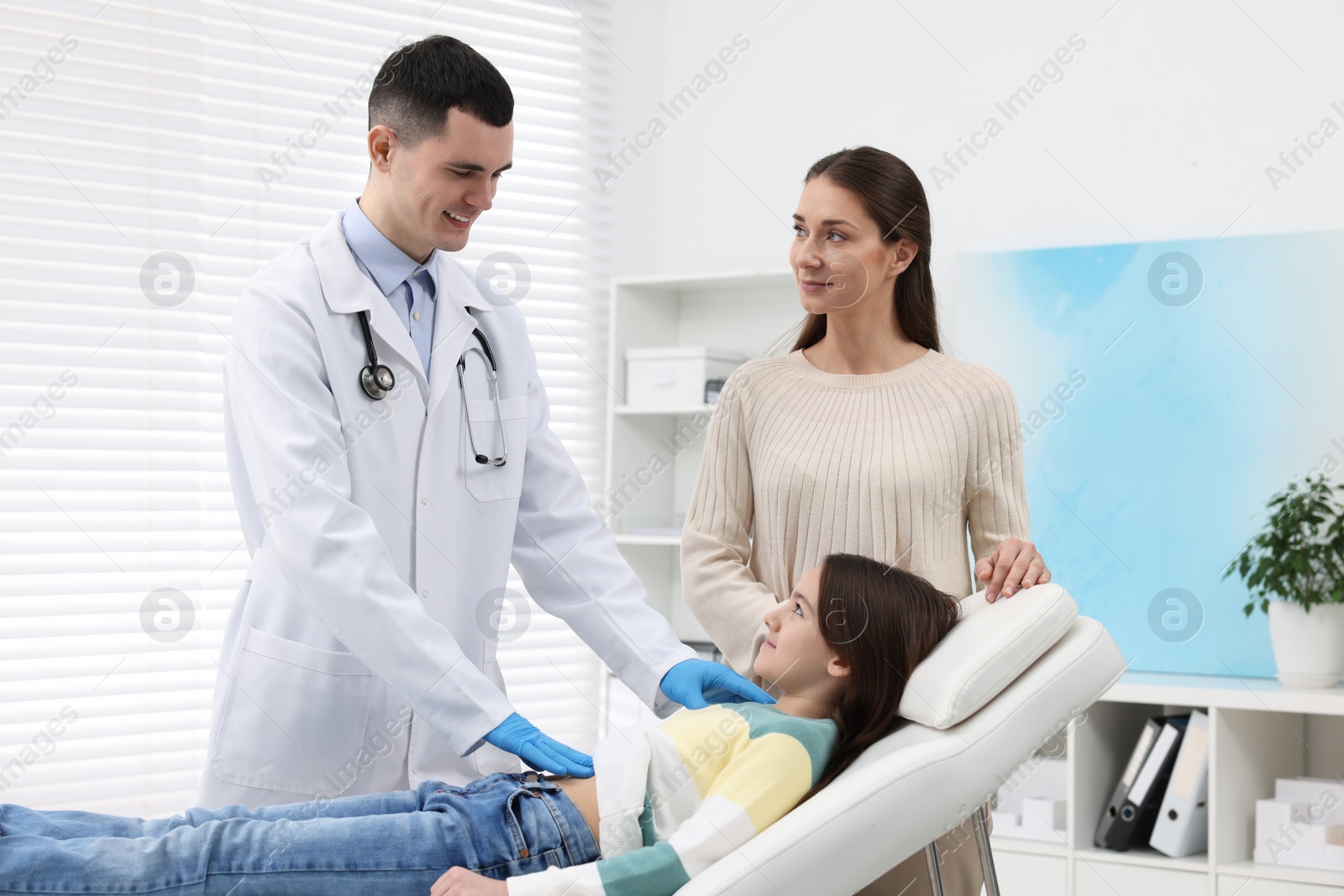 Photo of Gastroenterologist examining girl with stomach ache on couch in clinic