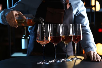 Photo of Bartender pouring rose wine from bottle into glass at table indoors, closeup