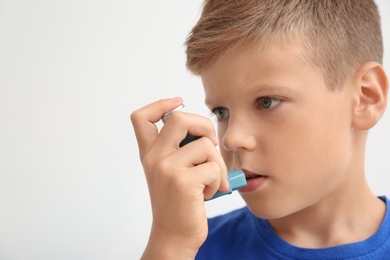 Little boy using asthma inhaler on light background