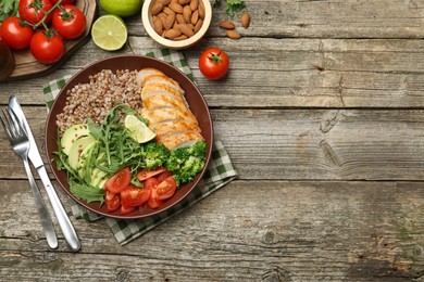 Healthy meal. Tasty products in bowl, ingredients and cutlery on wooden table, flat lay. Space for text