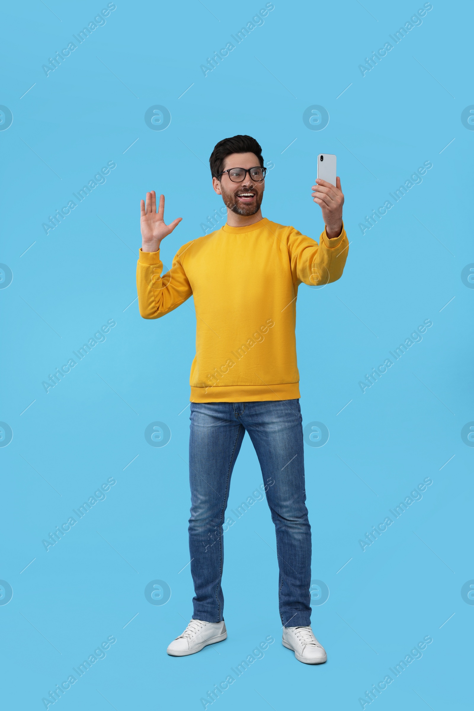 Photo of Smiling man taking selfie with smartphone on light blue background