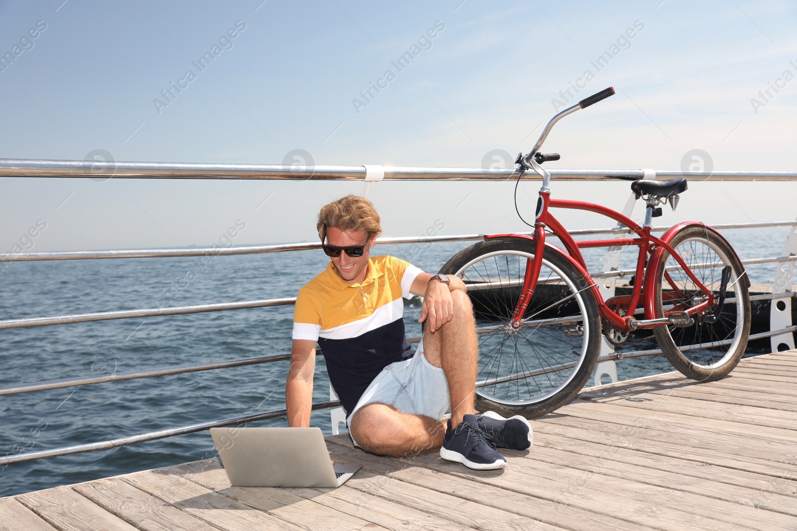 Photo of Attractive man with laptop and bike near sea on sunny day