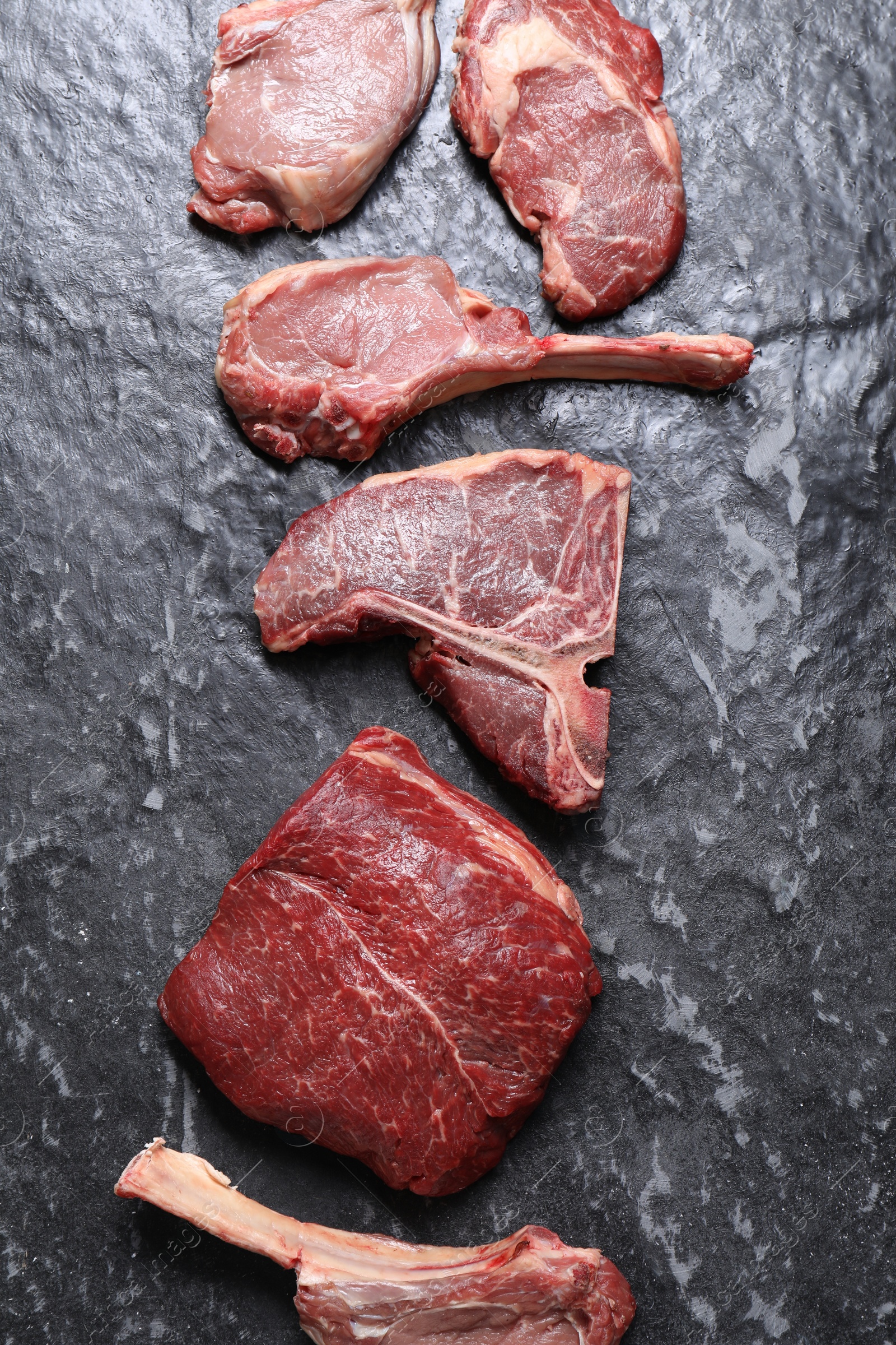 Photo of Fresh raw beef cuts on grey textured table, flat lay