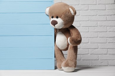 Photo of Cute teddy bear near light blue wooden wall against brick background, space for text