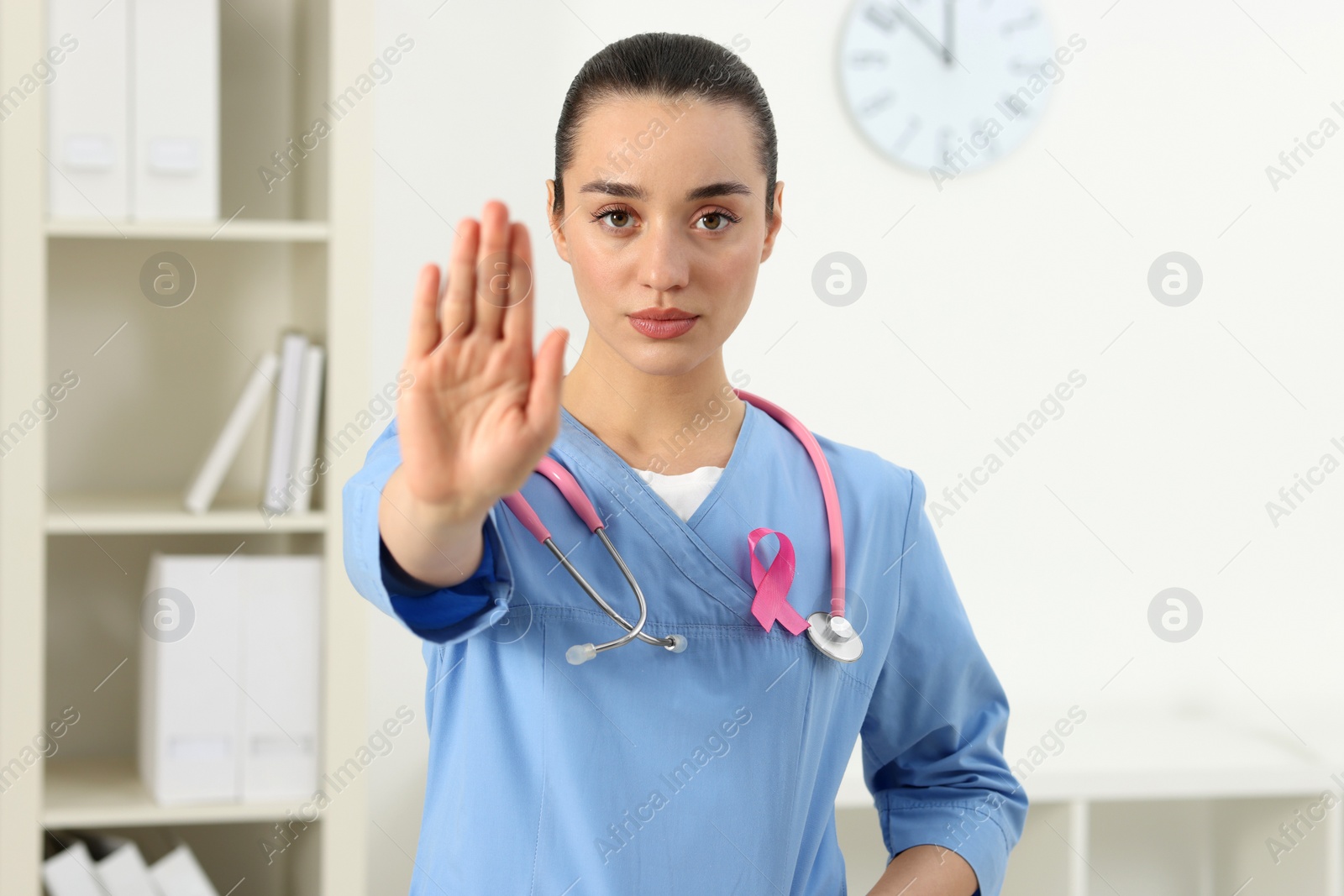 Photo of Mammologist with pink ribbon showing stop gesture in hospital. Breast cancer awareness